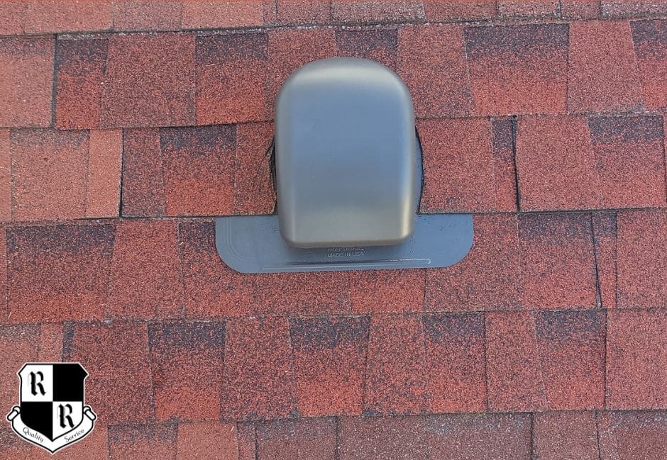 Gray metal roof vent sitting on red asphalt shingles; logo badge visible in the lower-left corner of the image.