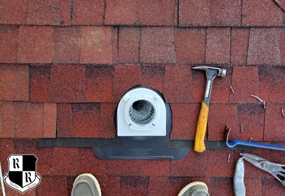 On a red shingled roof, a white vent boot is installed with a hammer, pry bar, and pliers nearby; worker's shoes visible at bottom.
